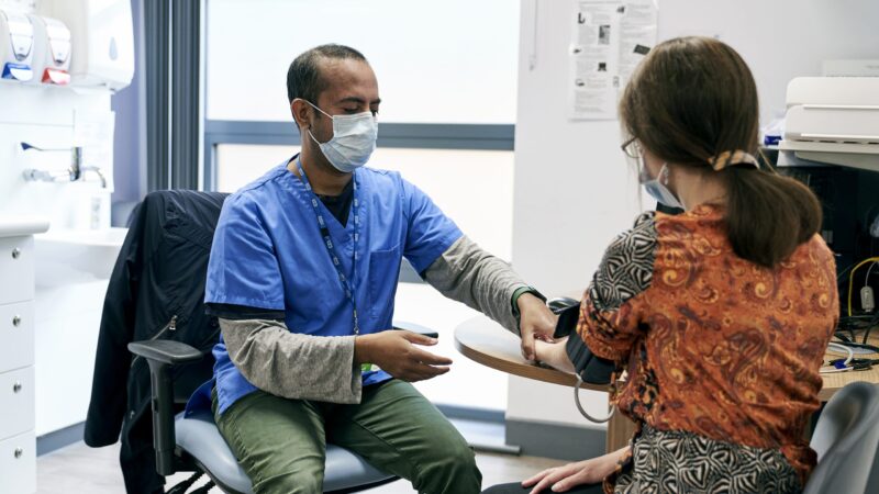 A GP measuring a patient's blood pressure in a consultation room